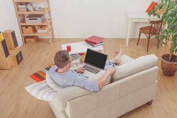 Top view of handsome man lying on sofa and looking at laptop computer. Businessman working from home.