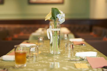 A small glass vase of white flowers on a green table at a wedding reception.