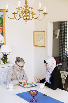 Young female home caregiver with senior woman playing ludo at home