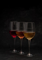 Red, pink and white wine in glasses on black grunge background