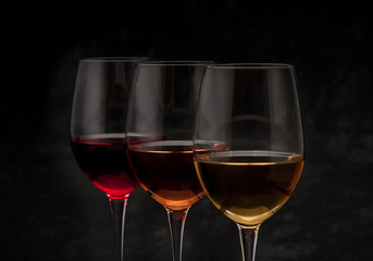 Red, pink and white wine in glasses on black grunge background