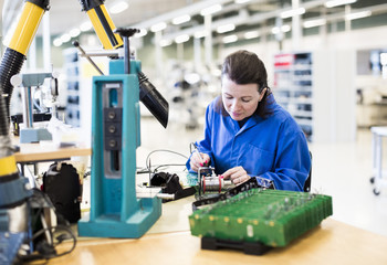 Mid adult female electrician working on circuit board at desk in industry