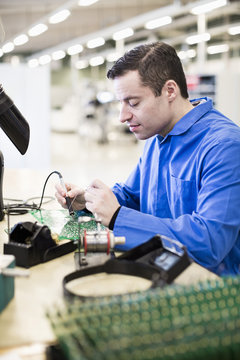 Mature male technician soldering circuit board at desk in industry