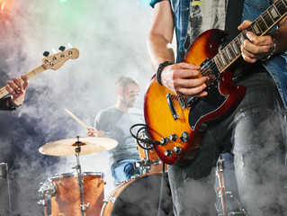 Rock band performs on stage. Guitarist, bass guitar and drums. Guitarist in the foreground. Close-up. - 113340274