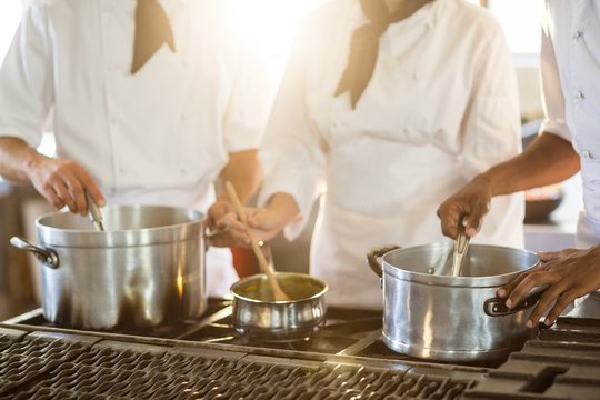 Mid Section Of Chefs Stirring In Cooking Pot