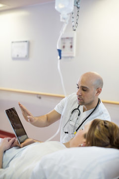 Mid adult male doctor explaining over digital tablet to patient lying on bed in hospital ward