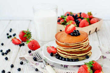 
easy hearty and healthy breakfast , American pancakes with berries , blueberries and strawberries with milk on a wooden background
