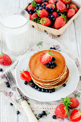 
easy hearty and healthy breakfast , American pancakes with berries , blueberries and strawberries with milk on a wooden background