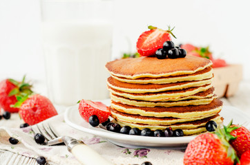 
easy hearty and healthy breakfast , American pancakes with berries , blueberries and strawberries with milk on a wooden background