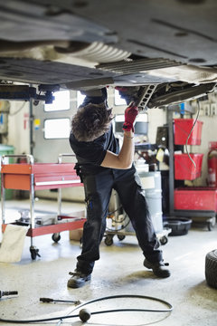 Young mechanic repairing car from below at auto repair shop