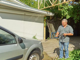 Man washing his silver car near house.
