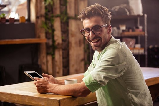 Happy hipster man posing for camera while using tablet