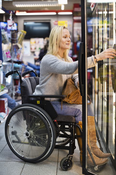 Disabled woman in wheelchair at refrigerated section of supermarket
