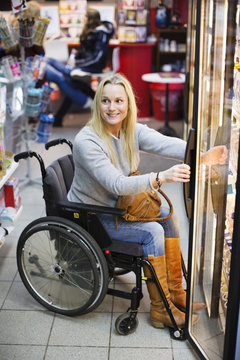 Happy disabled woman in wheelchair at refrigerated section of supermarket looking away