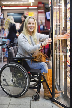 Portrait of happy disabled woman in wheelchair at refrigerated section of supermarket