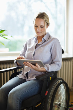 Disabled woman using digital tablet while sitting in wheelchair at home