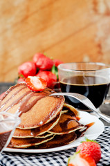 
easy hearty and healthy breakfast , American pancakes with strawberries and chocolate with coffee on a wooden background