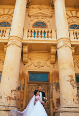 Romantic elegant newlywed couple posing near baroque column castle