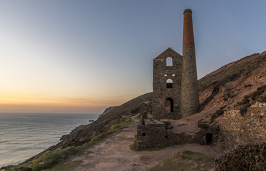 The ruin of a Cornish tin mine, on the edge of a cliff, with the sun setting into the ocean behind...