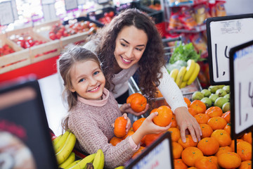 Mother and small pretty daughter buying citrus fruits