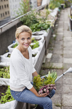 Portrait of happy young woman with freshly harvested vegetables at urban garden