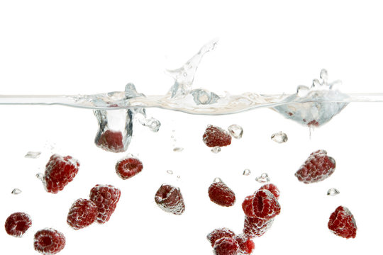 Fresh raspberries falling into water against white background