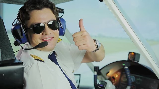 Happy male pilot in sunglasses smiling at camera, making thumbs up hand sign