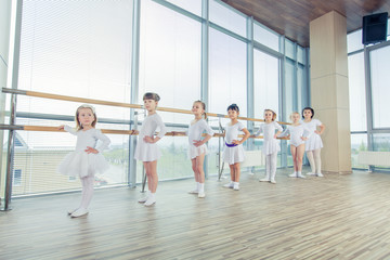 Fototapeta premium Group of seven little ballerinas standing in row and practicing ballet using stick on the wall
