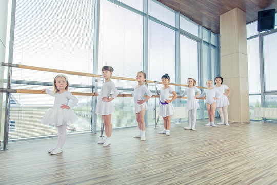 Group of seven little ballerinas standing in row and practicing ballet using stick on the wall