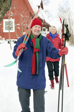 Two people outdoors carrying skis