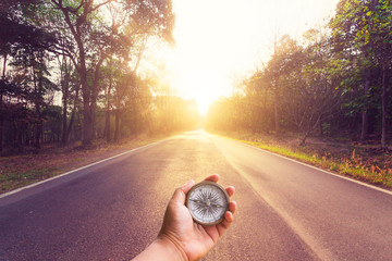 Hand holding compass on empty asphalt road and sunset.