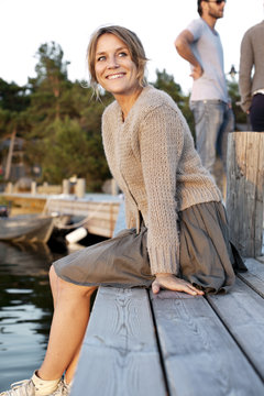 Blond mid adult woman sitting on pier with friends in background