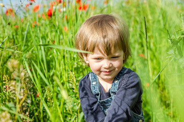 Little charming girl baby walking on the poppy field among the grass