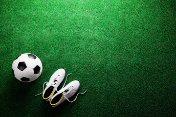 Soccer ball and cleats against green artificial turf, studio sho - Powered by Adobe
