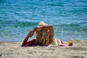 Blond woman sunbathing on beach, enjoying cold coffee frappe and looking at sea