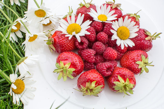 strawberry raspberries on a white plate on the grass with daisies