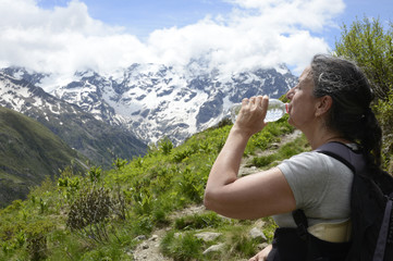 Naklejka premium Femme sur un chemin de montagne dans le parc national des Écrins buvant un peu d'eau