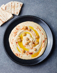 Hummus, chickpea dip, with spices and pita, flat bread in a black plate on grey stone background
