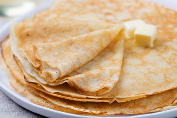 Thin crepes or pancakes with butter, honey and sour cream on a rustic textile background