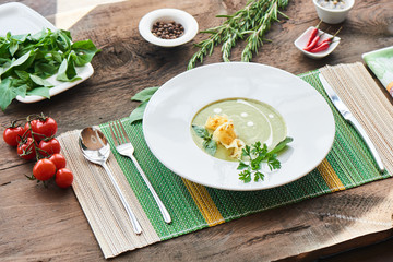 Healthy dinner soup with zucchini in a white plate on a wooden table