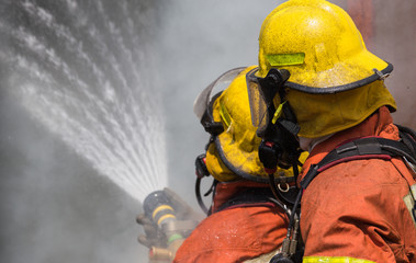  two firemen in helmet and oxygen mask spraying water to fire su