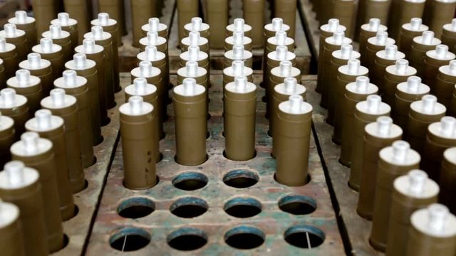 RPG explosive elements of anti tank rocket-propelled grenades (RPGs, bazooka) near an assembly line in a munition factory. Working in dangerous conditions. Zooming out.