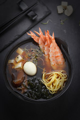 Japanese cuisine. Shrimp soup with ramen noodles over black background.