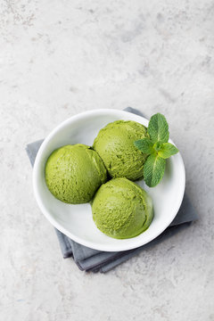 Green tea matcha ice cream scoop in white bowl on a grey stone background Copy space Top view.