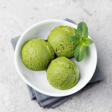 Green tea matcha ice cream scoop in white bowl on a grey stone background Copy space Top view.