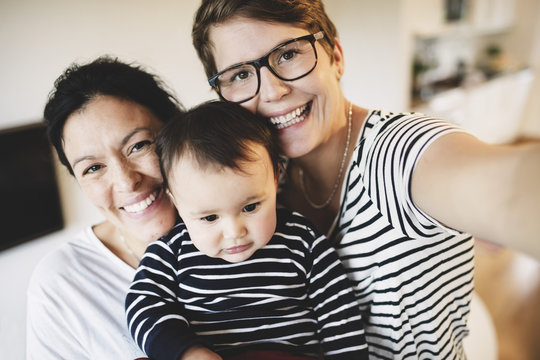 Portrait of smiling lesbian couple with toddler at home