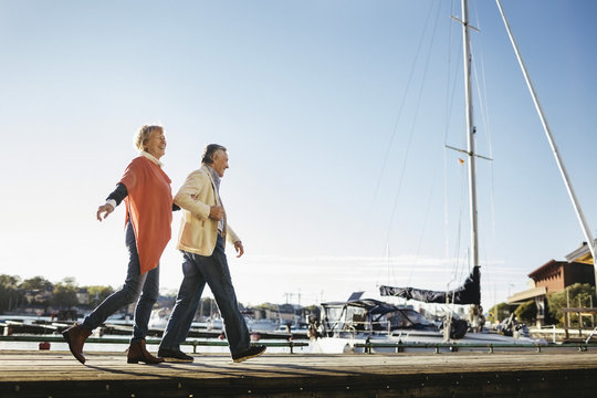 Full length of happy senior couple walking on pier against sky