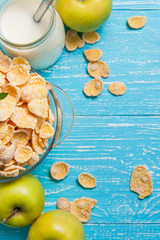 Bowl cereal on blue wooden table with fresh apple and milk near.