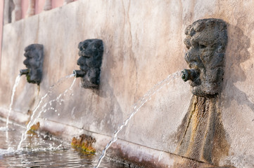 Fototapeta na wymiar Fountain with lava stone mascarons in one small village at the bottom of Mount Etna, Sicily