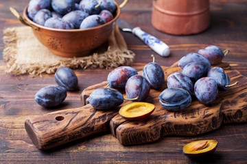 Fresh organic plums in copper bowl and on rustic wooden cutting board